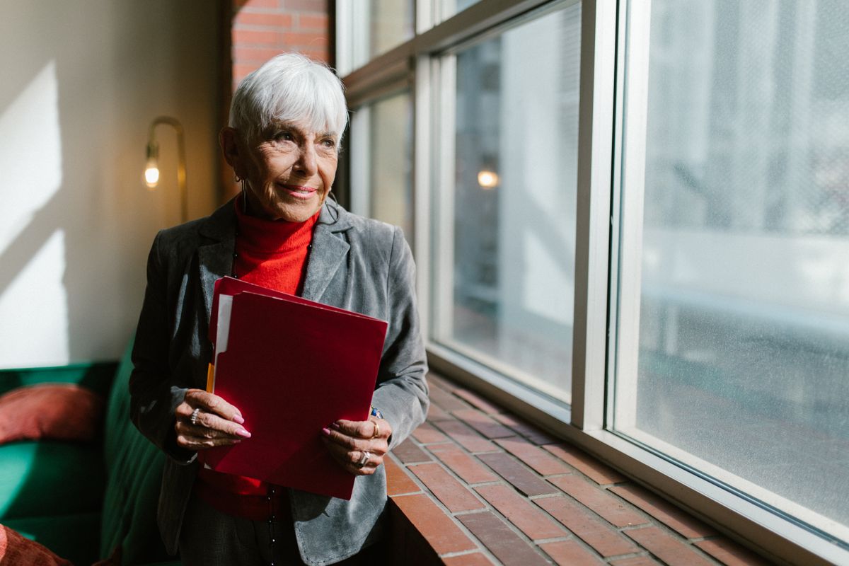 A confident woman smiling by a sunlit window, holding a folder
